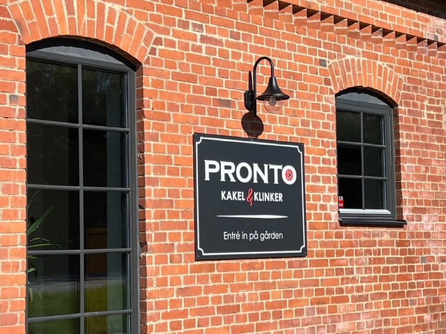 Pronto Kakel-skylten på tegelfasaden mot gatan, som visar vägen in på gården.