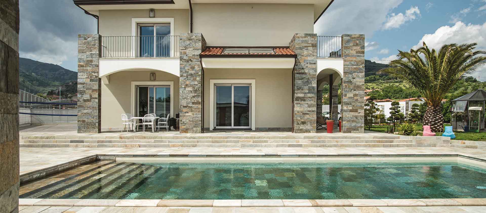 Villa med naturstensklädda fasadpartier, stenbelagd uteplats och pool.